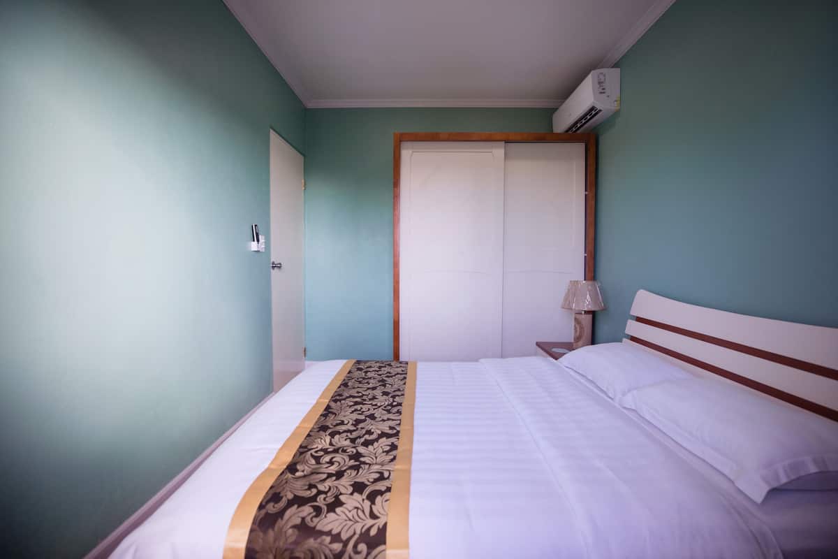 A bedroom with a bed, a nightstand, a lamp, and an air conditioning unit.