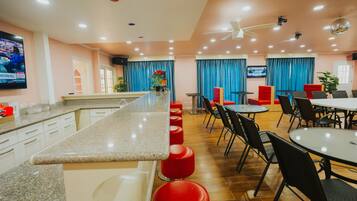 A modern kitchen with a long counter, red bar stools, and a dining area with tables and chairs.