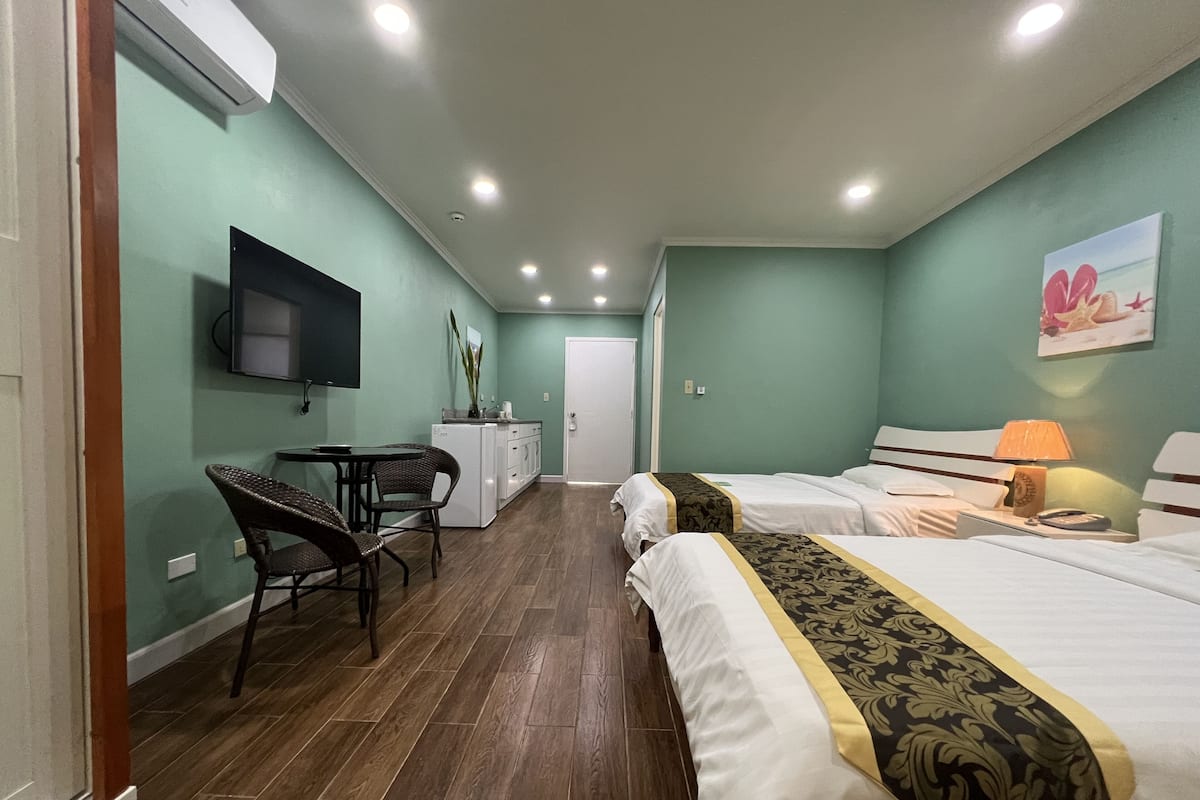 A hotel room with two beds, a dining area with a table and chairs, a TV mounted on the wall, and a door leading to another room.