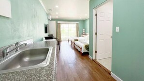 A hotel room with a kitchen area, a large window, and a door leading to another room. - Beach Garden Hotel (Saipan)