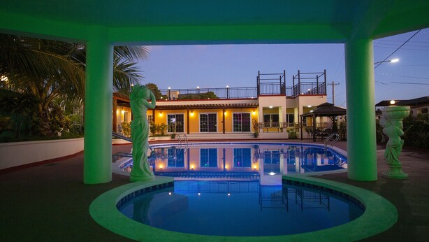 A hotel with a swimming pool, outdoor seating, and a well-lit building facade. - Beach Garden Hotel (Saipan)