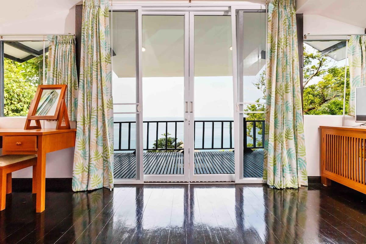 Ein Zimmer mit einem Holztisch, einem gerahmten Bild und Blick auf einen Balkon mit Geländer.