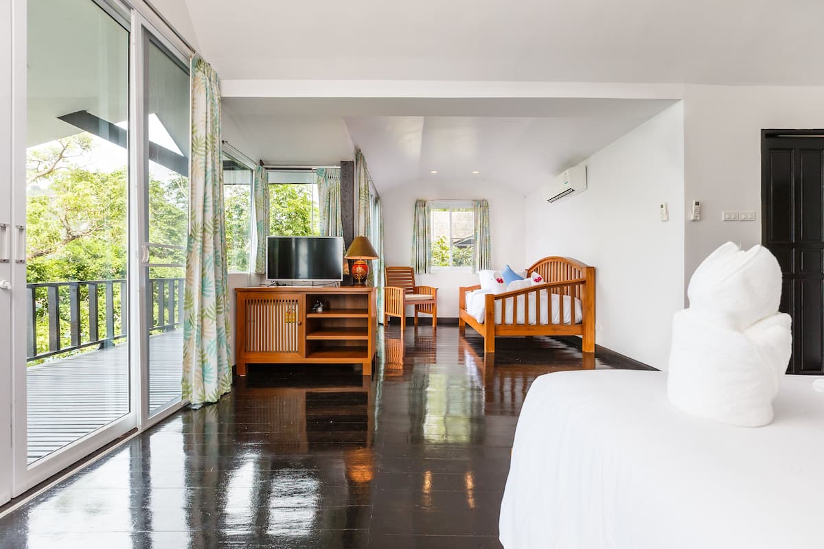 Ein Hotelzimmer mit einem großen Bett, einem Schreibtisch mit Fernseher, einem Sessel und Blick ins Grüne durch die Fenster.