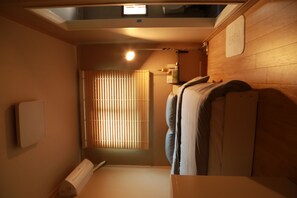 A compact hotel room with a skylight, a bed with a headboard, a bedside table, a window with blinds, and a wall-mounted air conditioning unit. - 88st GUESTHOUSE Jongno (Seoul)
