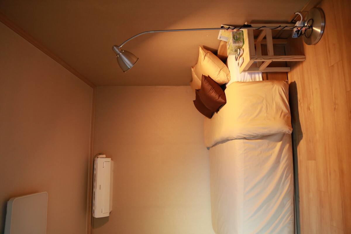 A small, cozy room with a bunk bed, a bedside table with a lamp, and a wall-mounted heater.