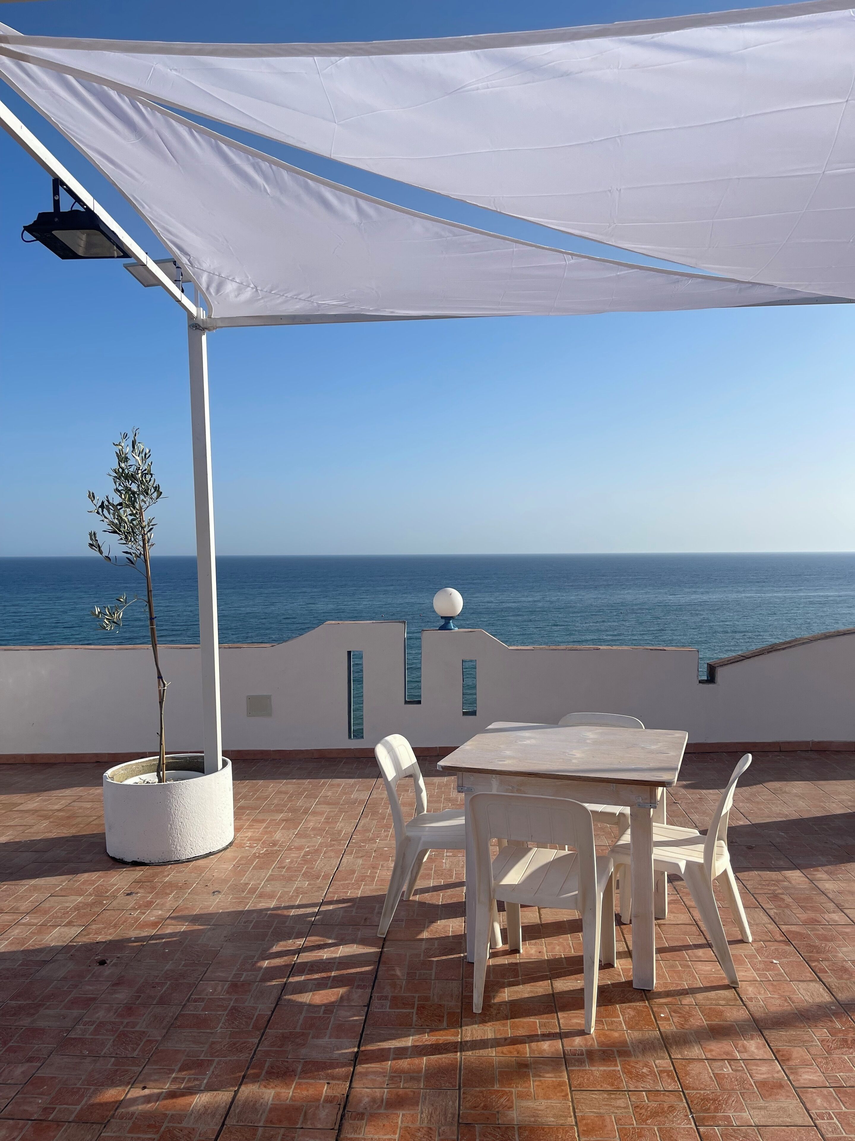 Eine Terrasse mit Tisch und Stühlen, einem Blumentopf und Blick aufs Meer.