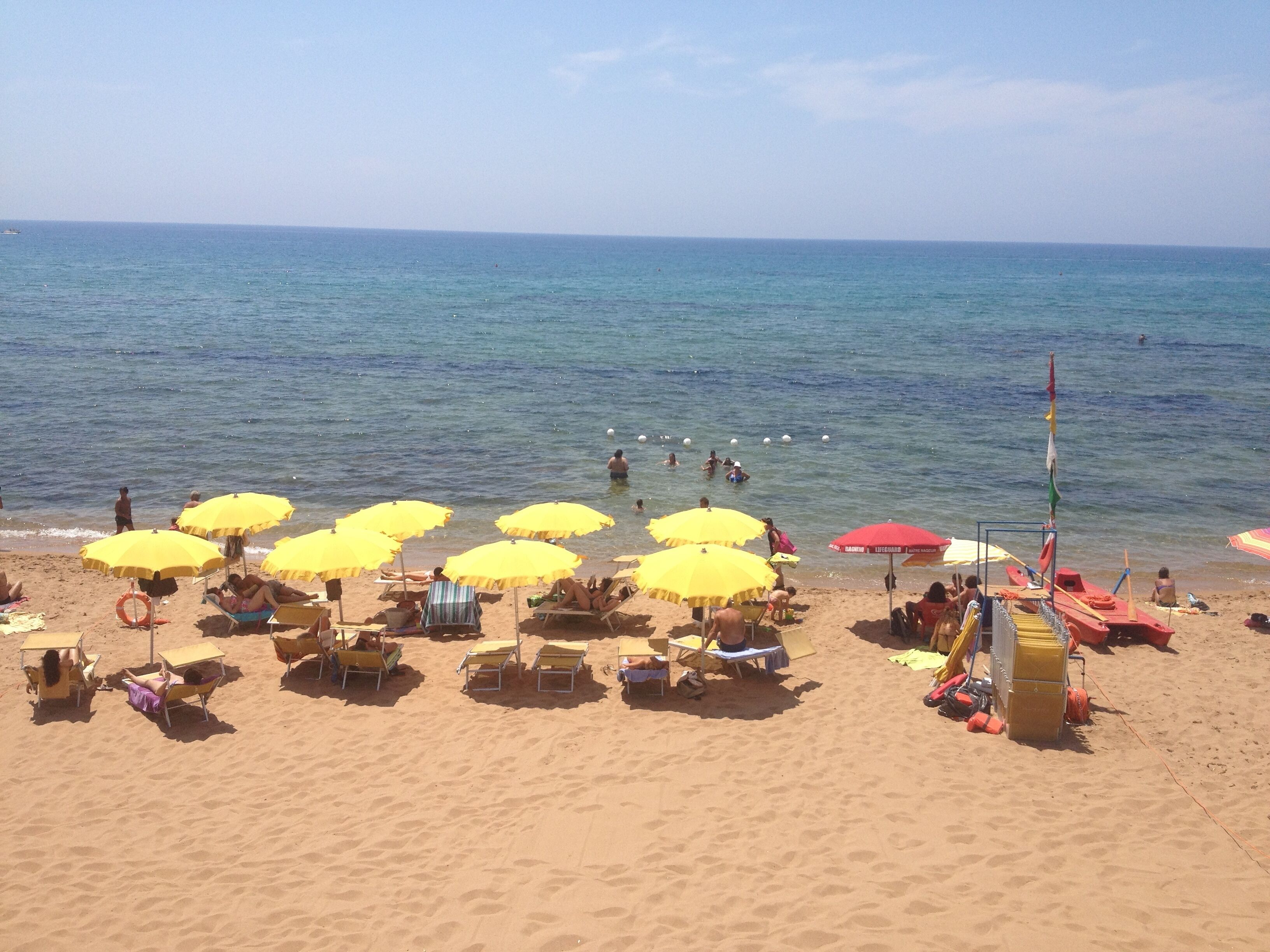 A beach with yellow and red umbrellas, sun loungers, and a lifeguard stand.