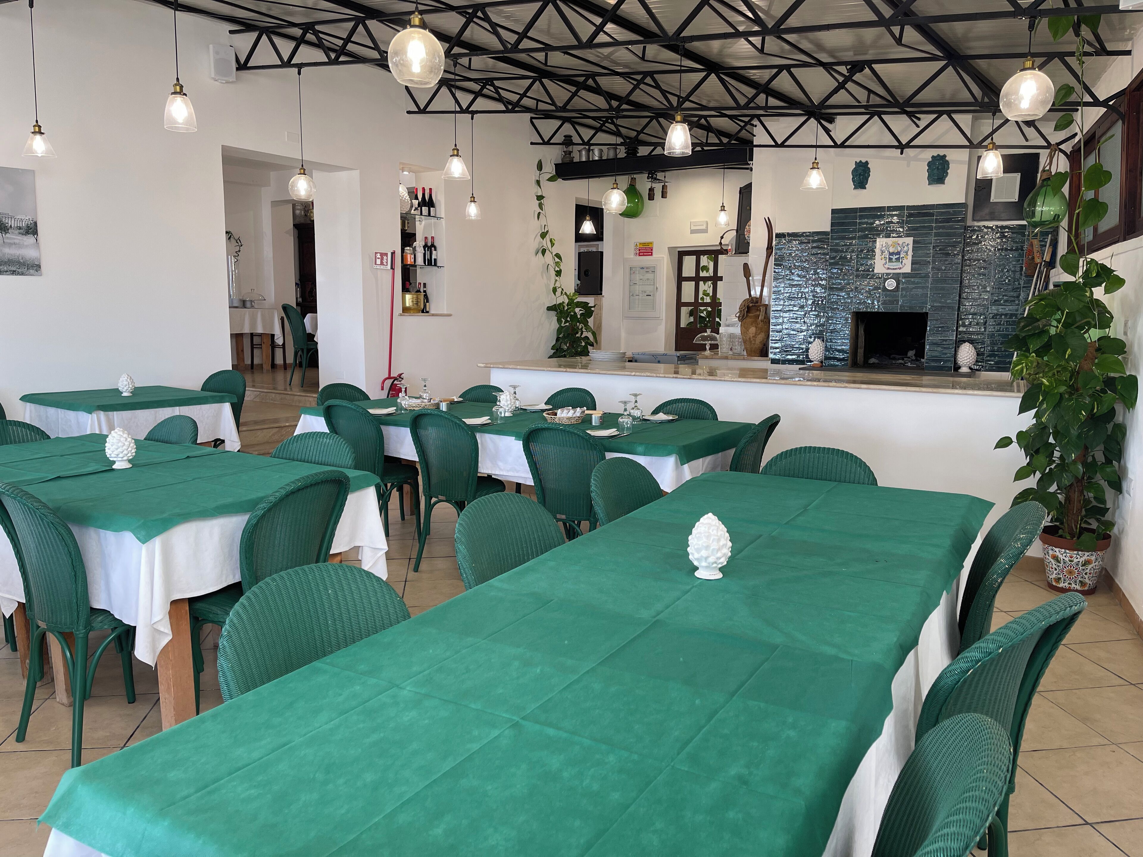 A restaurant with green tablecloths, wicker chairs, and hanging pendant lights.