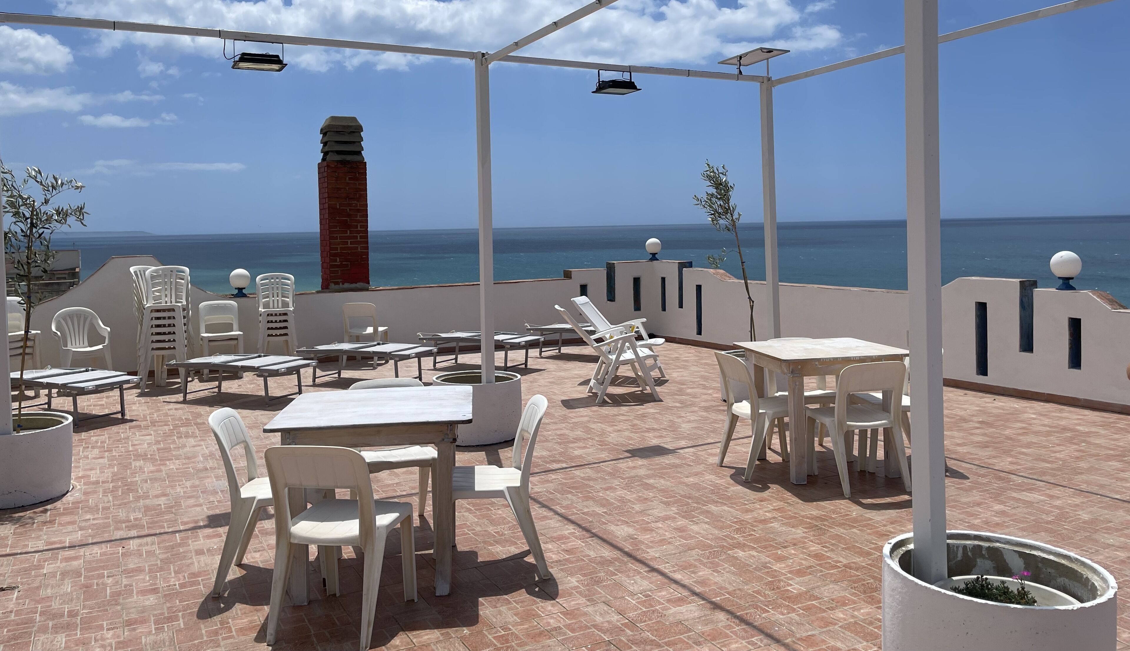An outdoor patio with white furniture, a brick chimney, and a view of the sea.