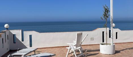 A terrace with sun loungers and a chair overlooking the sea.