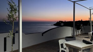 An outdoor patio with a table and chairs, a potted plant, and a view of the sea at sunset. - Hotel Miramare Garzia (Castelvetrano)
