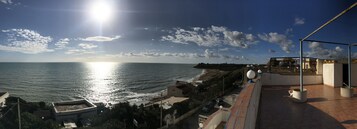 Vista costera con cielo despejado, mar iluminado por el sol y un edificio con balcón que da al océano.