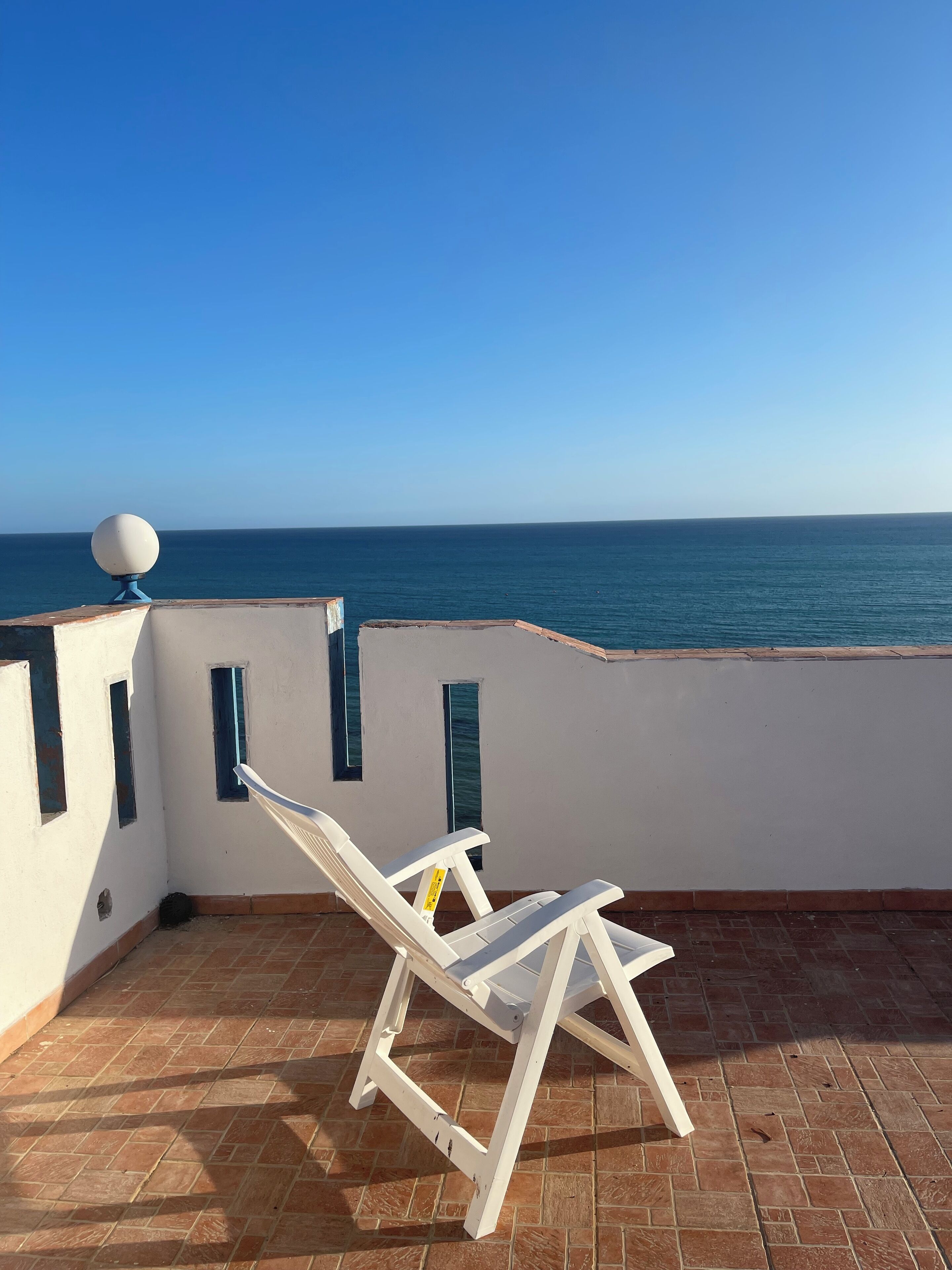 Una silla lounge blanca en un patio empedrado con vista a un cuerpo de agua.