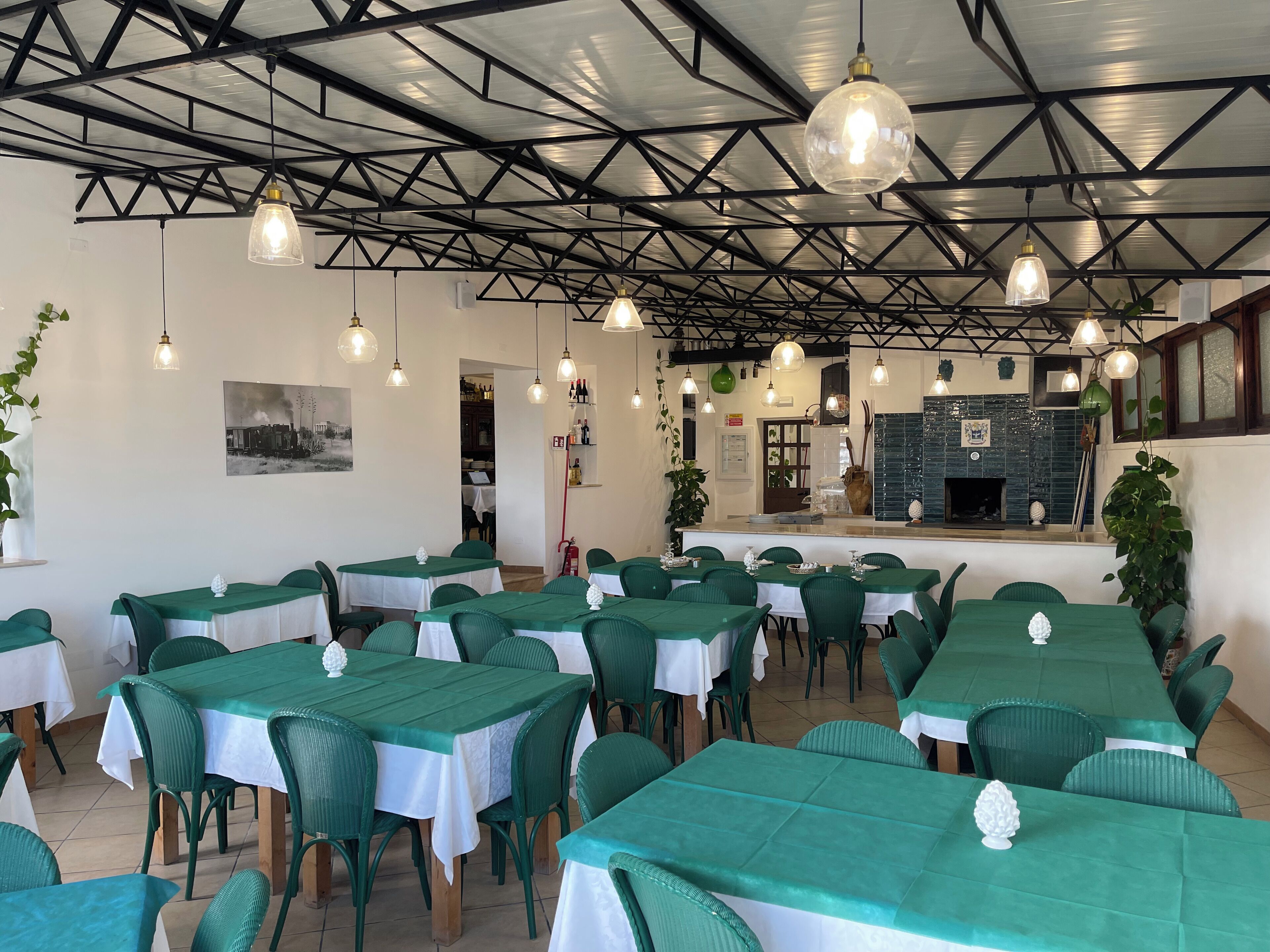 Un restaurant doté de nombreuses tables recouvertes de nappes vertes et de chemins de table blancs, avec un plafond de style industriel moderne, des poutres apparentes et des luminaires suspendus.