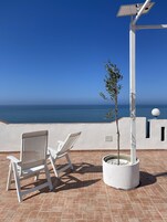 Una terraza con dos sillas blancas, un árbol en maceta y un panel solar.