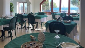 A restaurant with multiple tables covered in green tablecloths, white chairs, and a view of the sea through large windows. - Hotel Miramare Garzia (Castelvetrano)