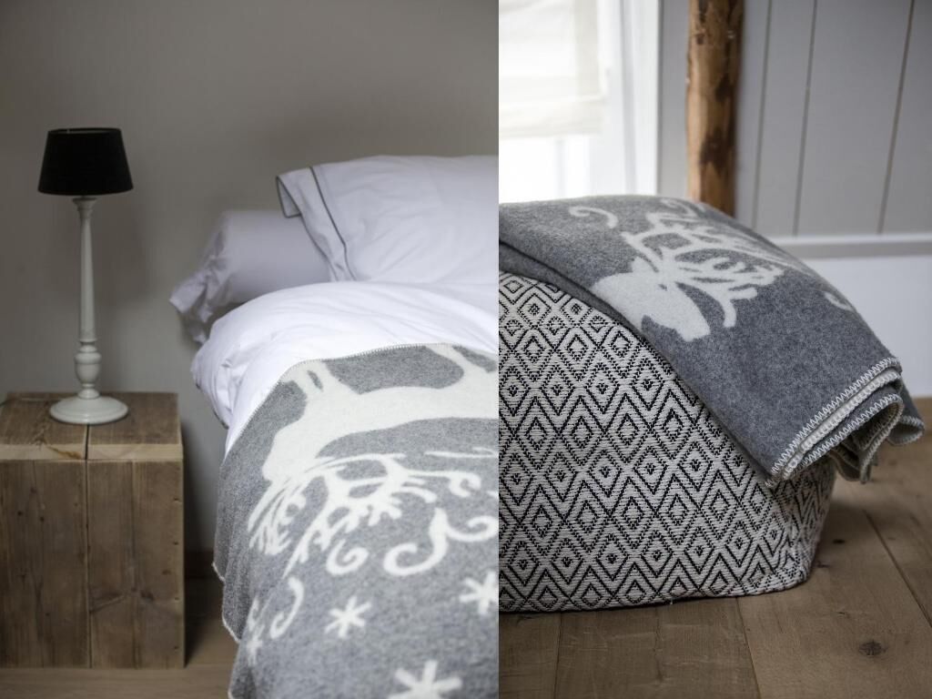 A bed with a white pillow and a grey blanket with a snowflake pattern.