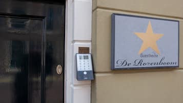 A black door with a keypad lock, a star-shaped sign with "Guesthouse De Rozenboom" text, and a small plaque above the door.