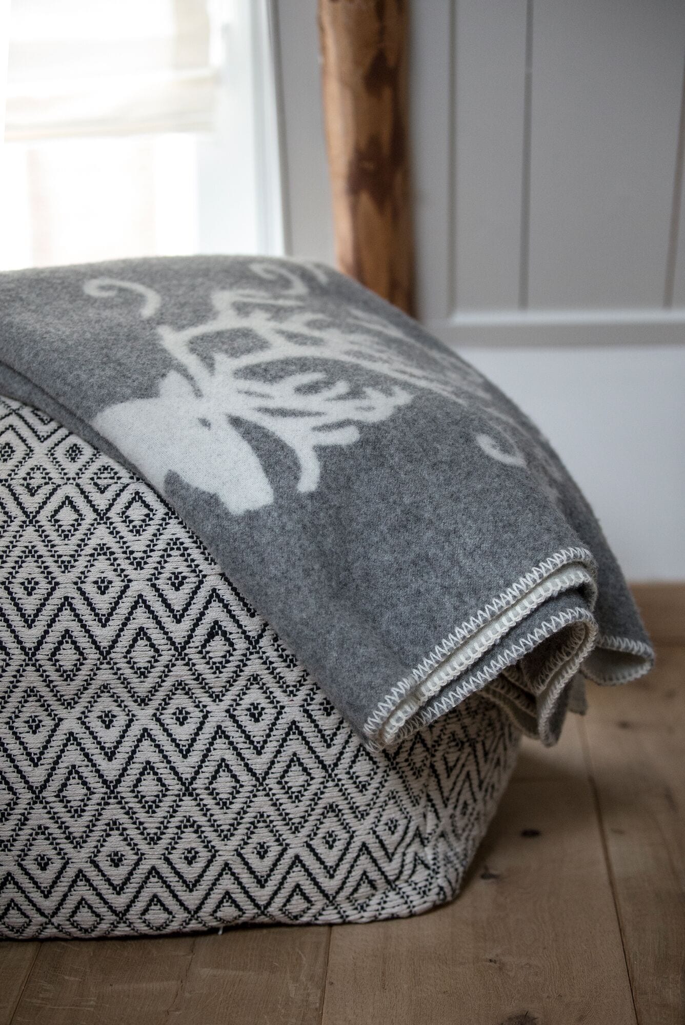 Un coussin aux motifs gris et blancs est posé sur un plancher en bois.