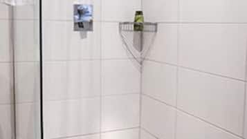 Et moderne brusebad med glasdør, indbygget hylde og brusearmatur i loftet.