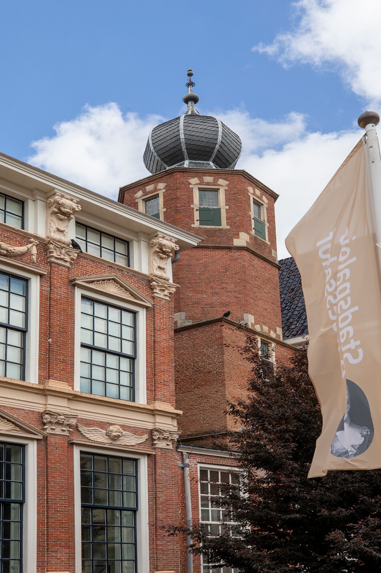 Ein historisches Gebäude mit einem markanten Turm, der eine runde Kuppel und einen Wetterhahn zeigt.