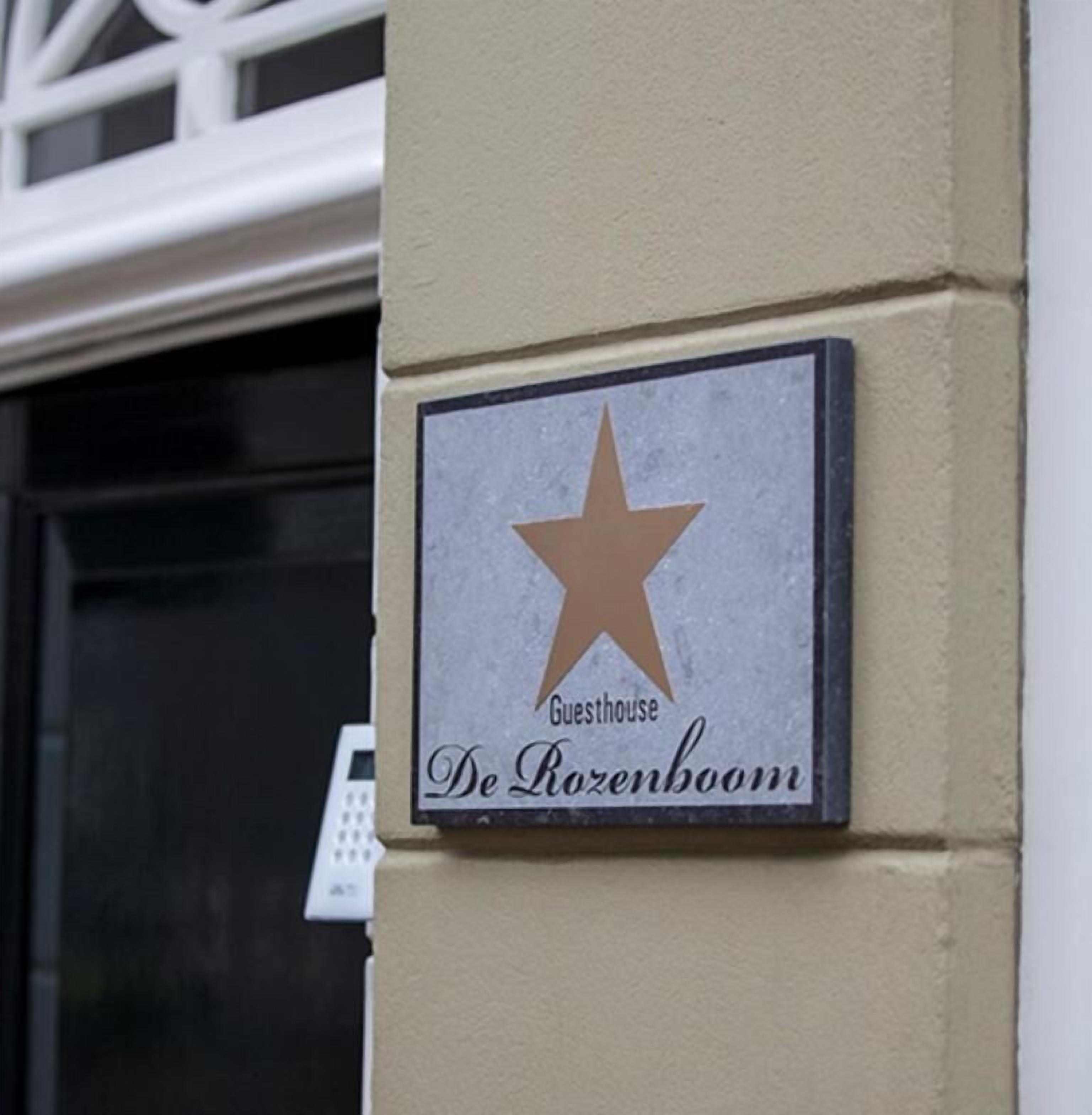 Een bord met een ster en de tekst 'Guesthouse De Rozenboom' op een gevel.