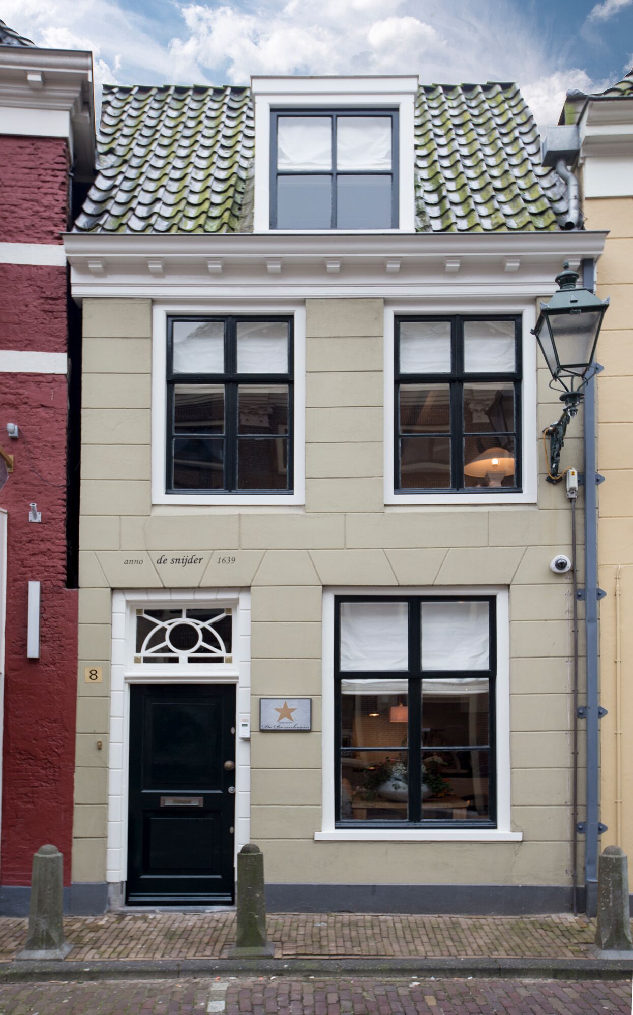 Een gebouw met twee verdiepingen, een zwarte deur, een bord waarop staat 'Anno de Snijder 1639' en een lantaarnpaal aan de rechterkant.