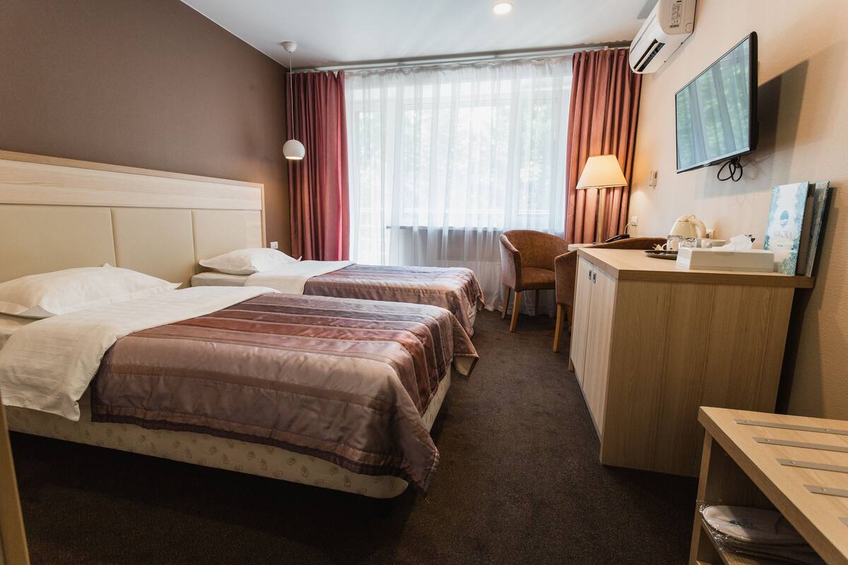 Hotellihuone, jossa on kaksi sänkyä, työpöytä, tuoli, televisio ja ikkuna, jossa on verhot.