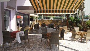 An outdoor patio area with wicker furniture, a striped awning, and a stone-tiled floor. - Rosella Hotels (Alanya)