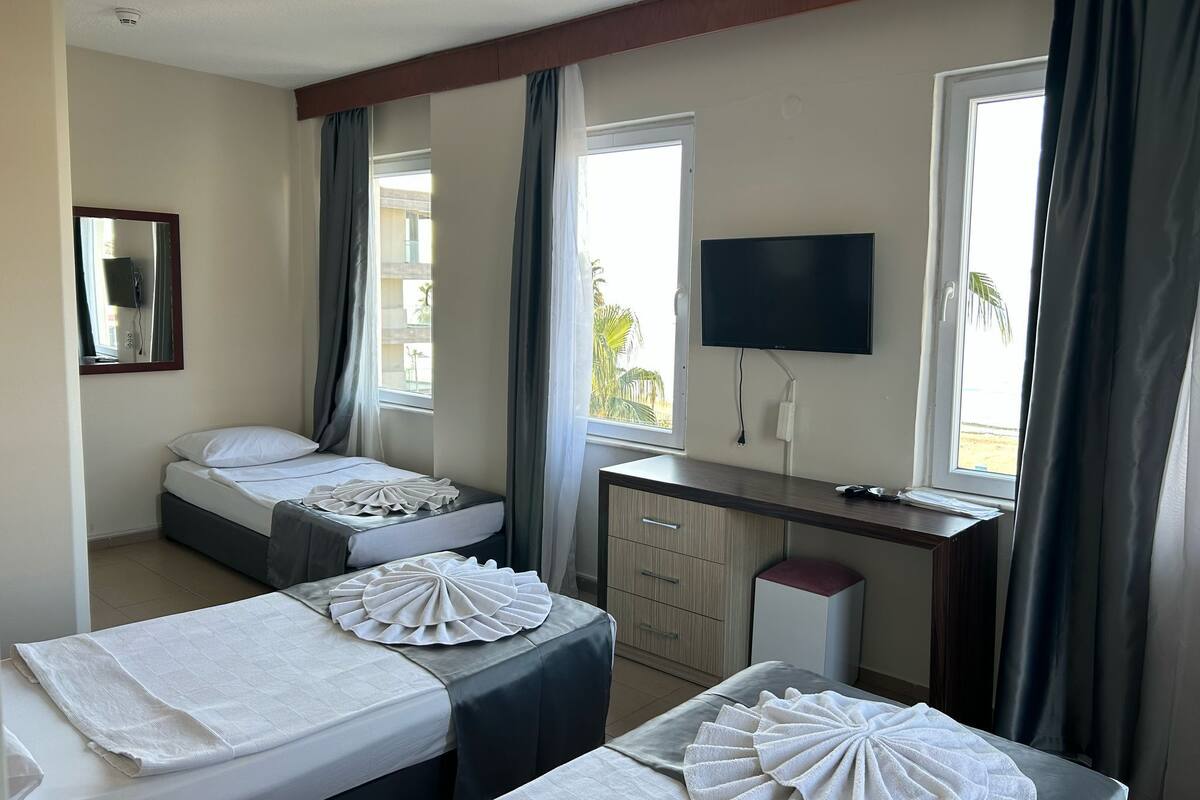 A hotel room with two beds, a desk, a TV, and a window with curtains.