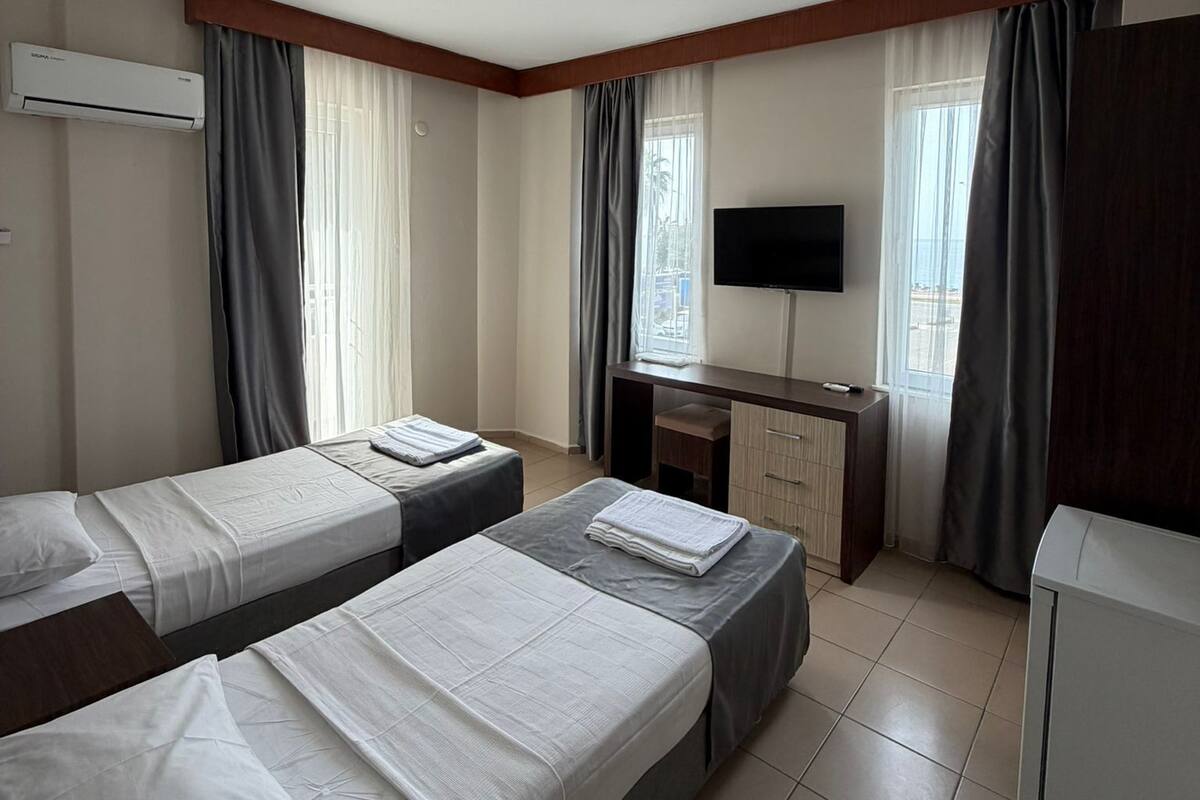 A hotel room with two beds, a desk, a TV, and an air conditioning unit.