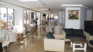 A modern lounge area with sofas and armchairs, a coffee table, and a large window offering a view of the outside. - Rosella Hotels (Alanya)