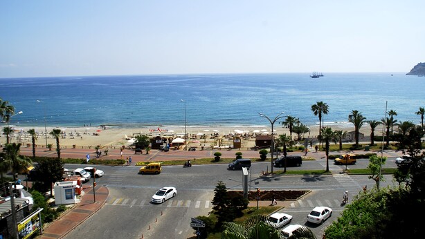 A coastal road with a beach in the background, a clear sky, and a few vehicles on the road. - Rosella Hotels (Alanya)