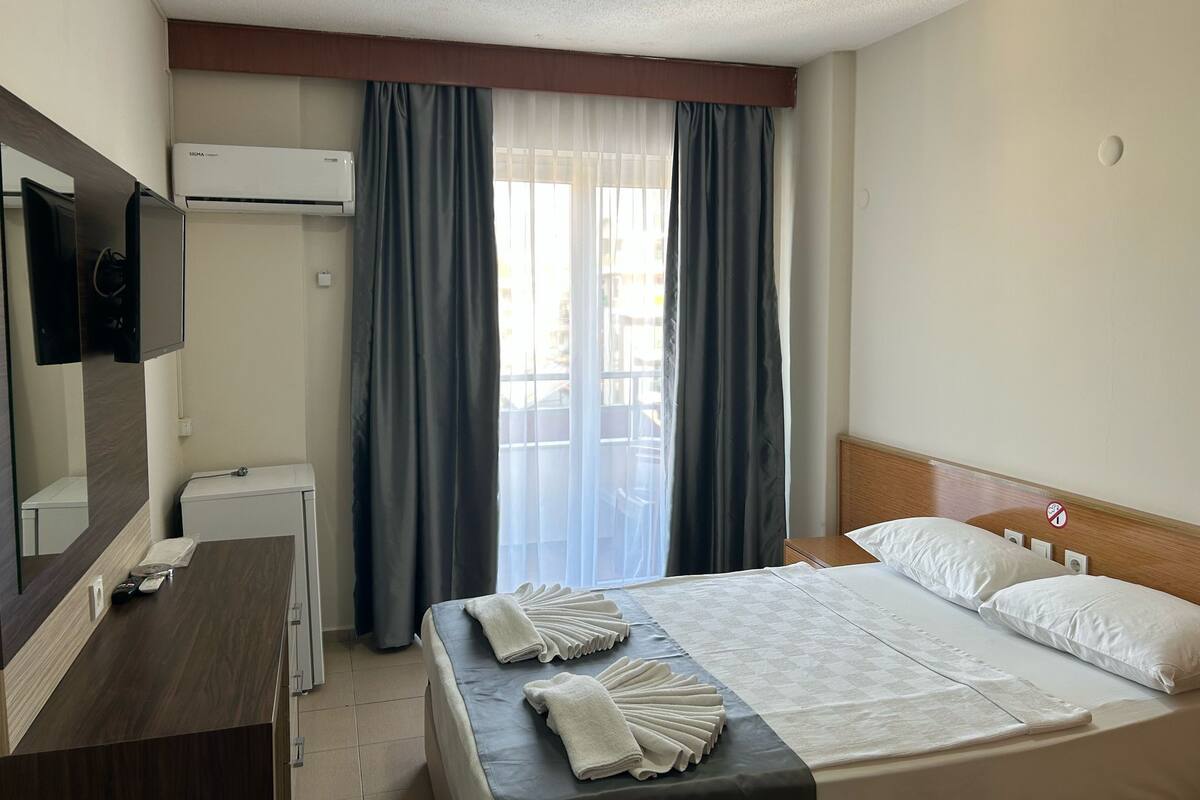 A hotel room with a bed, a desk, a TV, and an air conditioning unit.