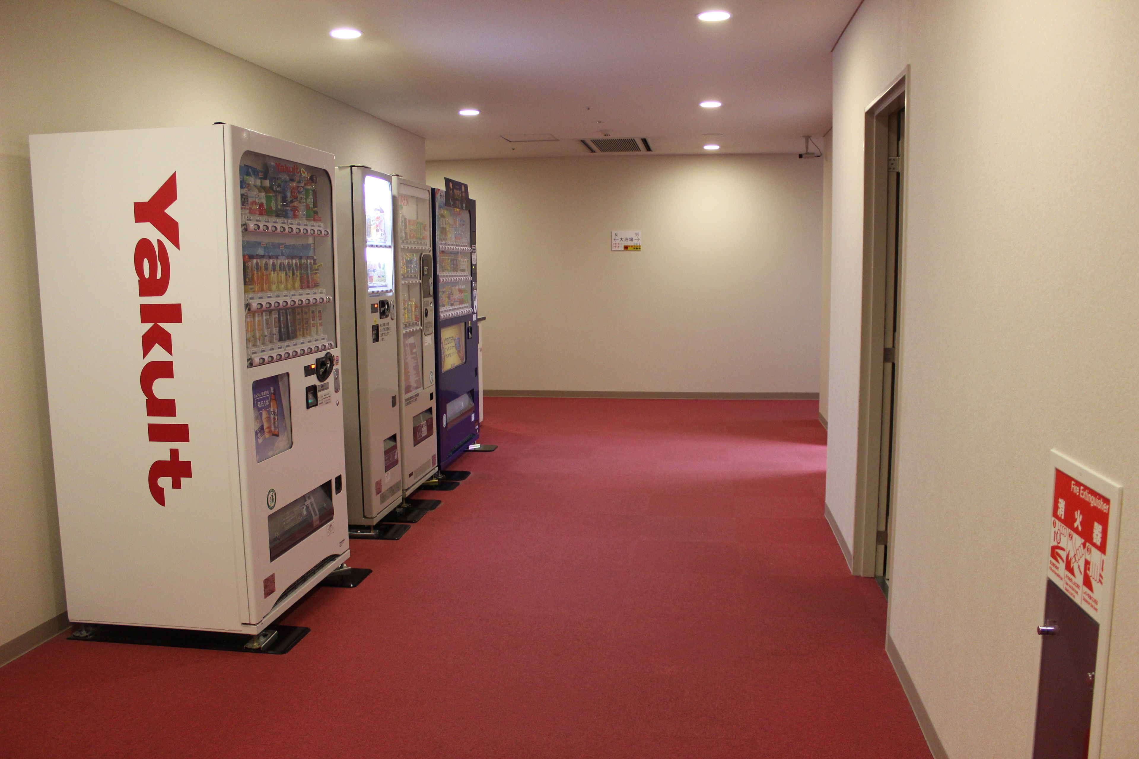 A hallway with vending machines labeled 'Yakult' and a red carpet.