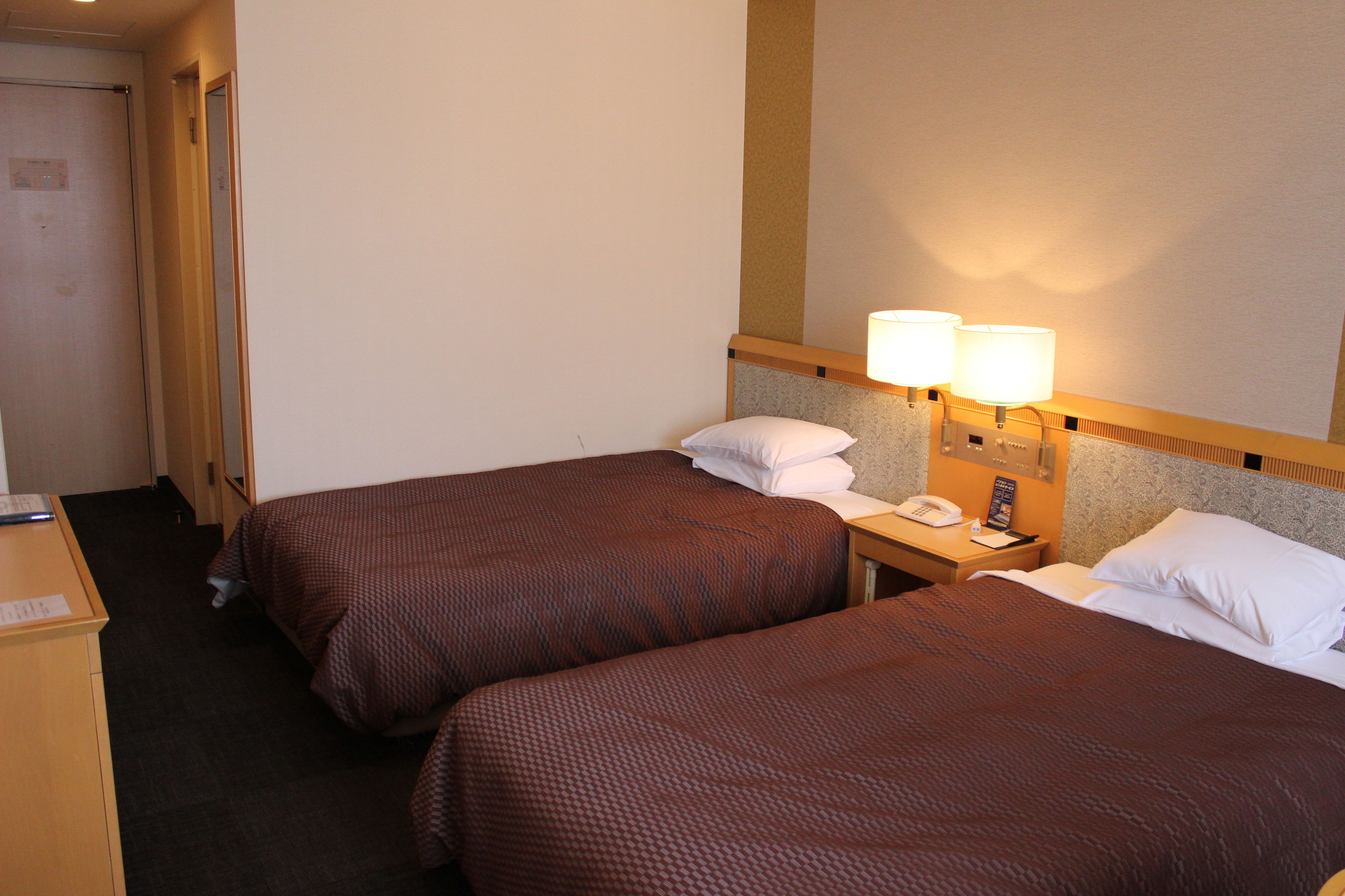 A hotel room with two beds, a desk, and a telephone.