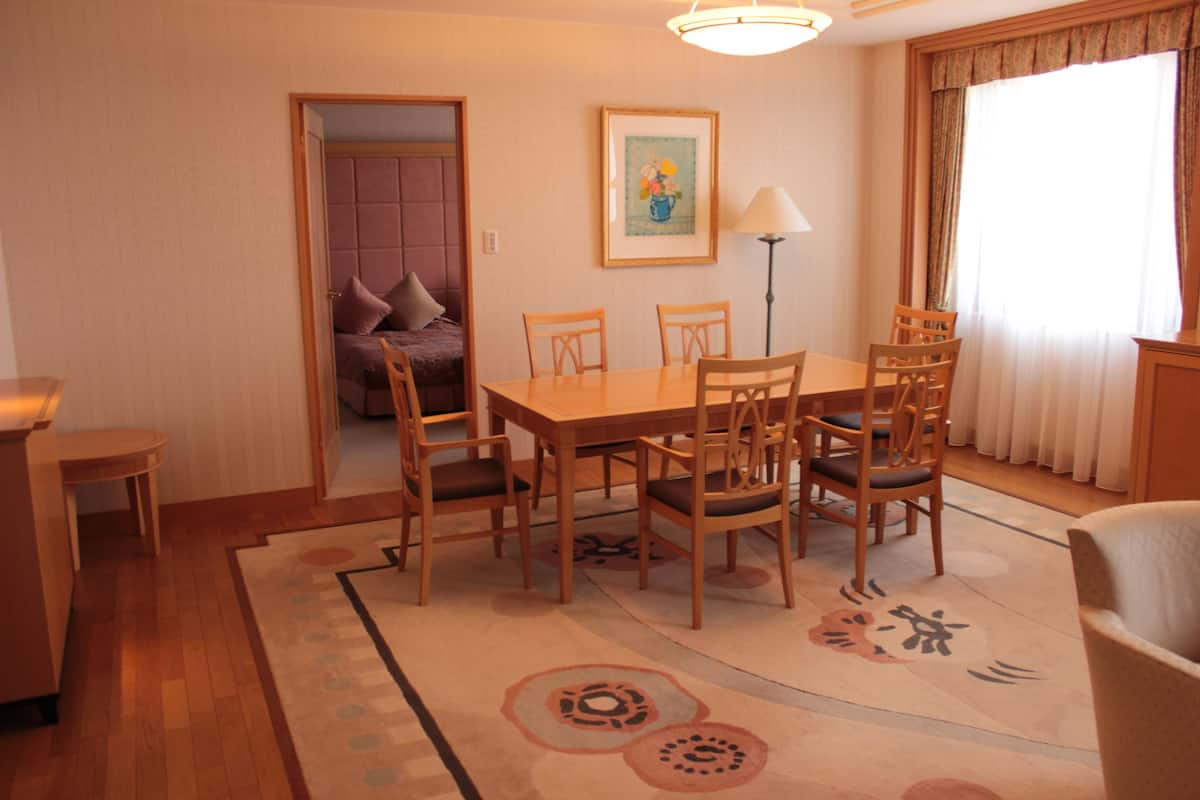 Un área de comedor con una mesa y sillas de madera, un tapete con diseño circular, un cuadro en la pared y una lámpara.