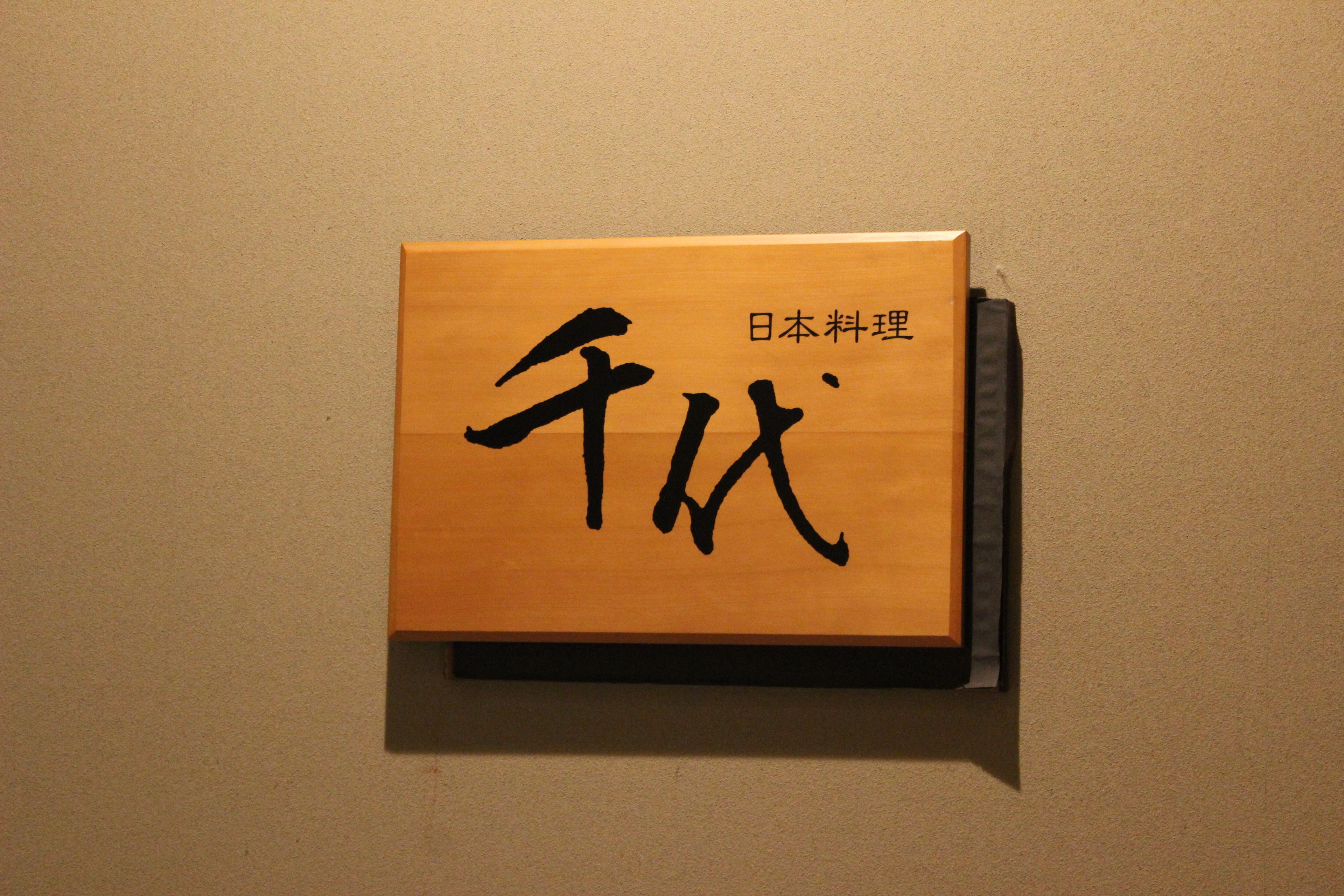 Eine Holzkiste mit japanischer Kalligraphie an einer beige farbenen Wand.