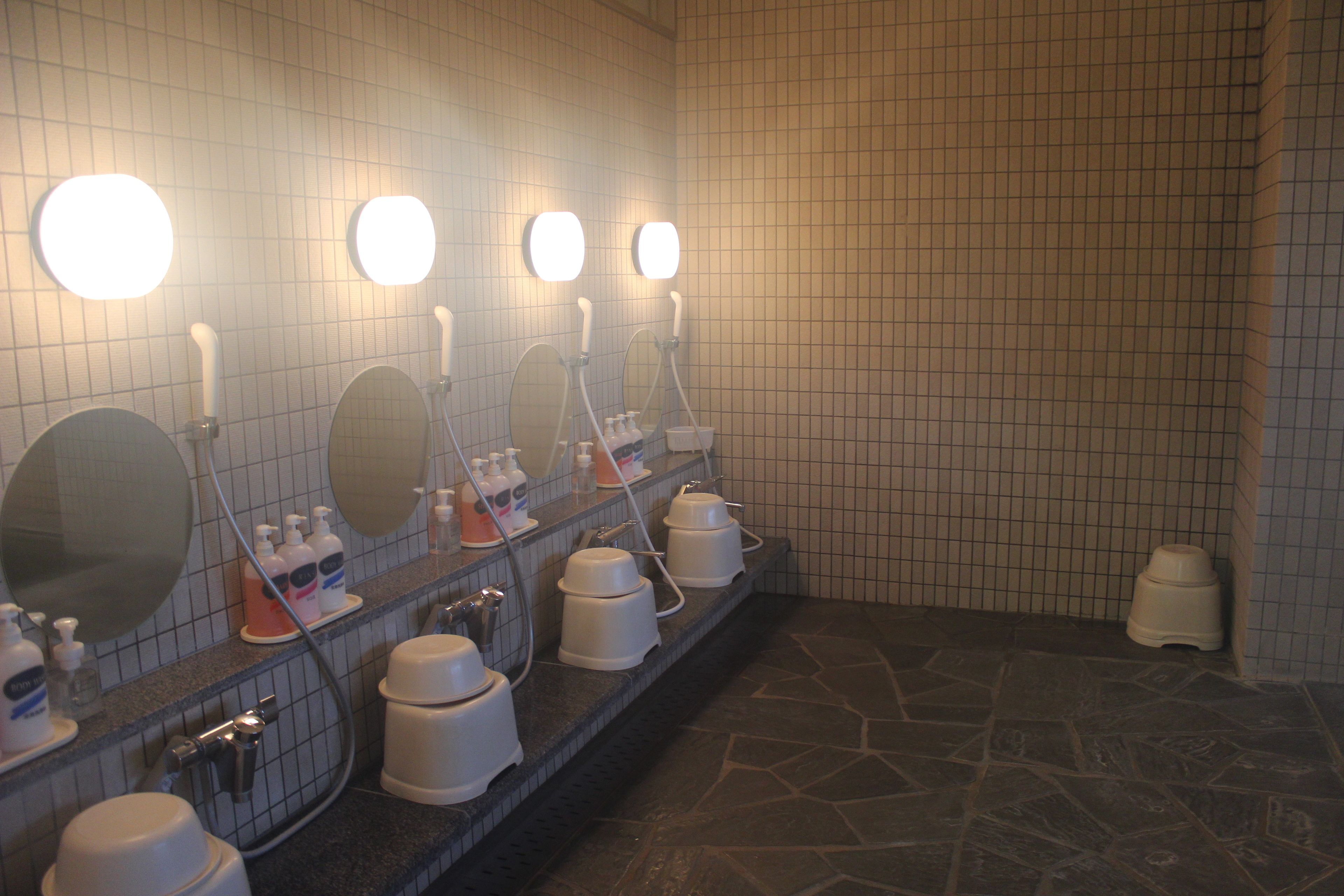 En offentlig toilet med flere håndvaske, spejle og håndtørrere.