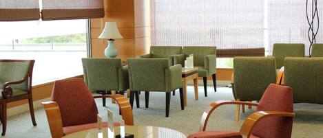A hotel lobby with green and red upholstered chairs, a round wooden table, and a lamp.