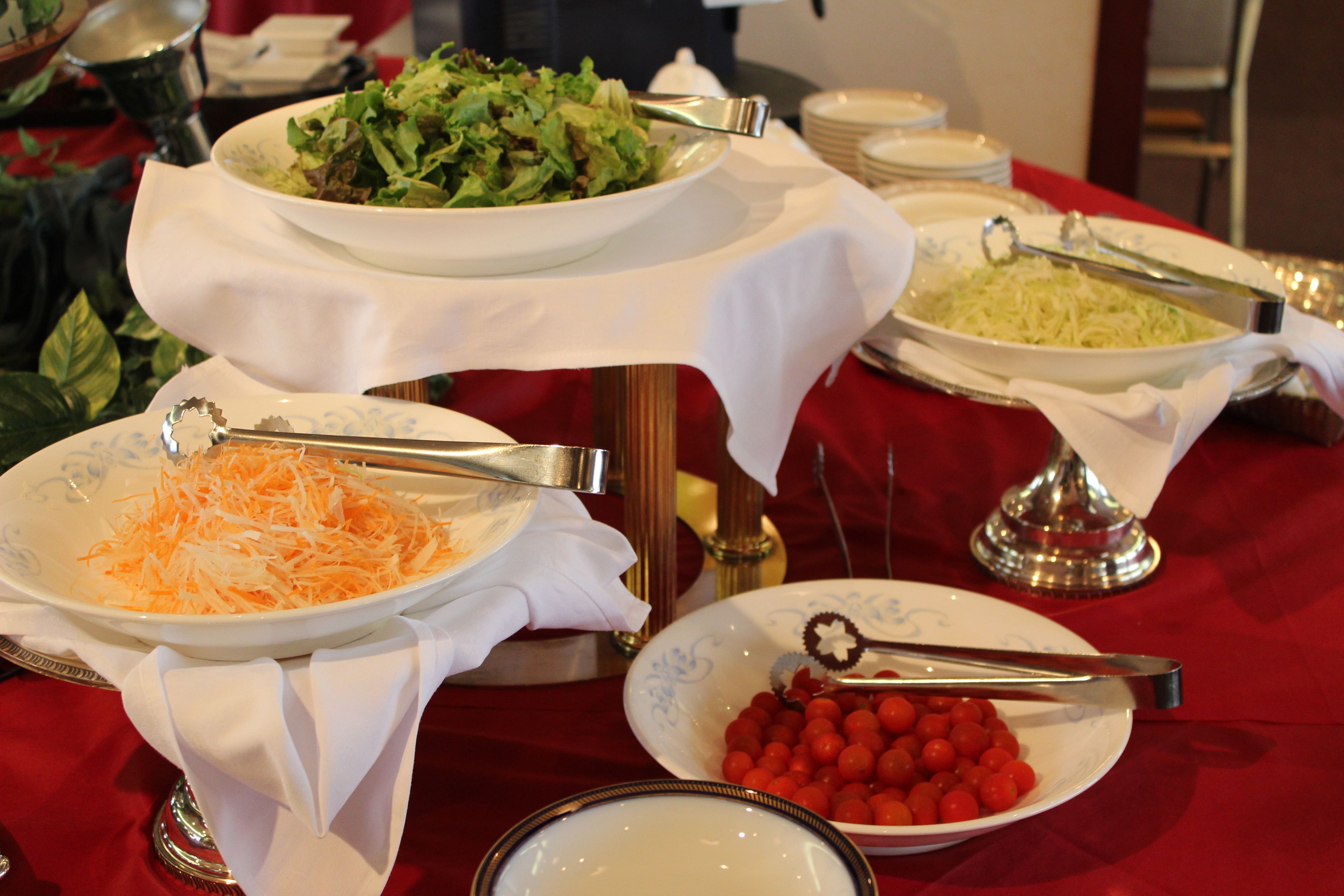 Un tavolo per buffet con diversi piatti, tra cui un'insalata, formaggio grattugiato e pomodorini.
