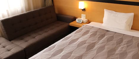 A hotel room with a bed, a sofa, a nightstand, and a wall-mounted lamp.