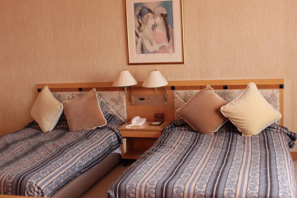 Habitación de hotel con dos camas, cada una con ropa de cama estampada, una mesita de noche con lámpara, teléfono y un cuadro en la pared.