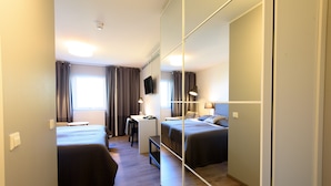 Een hotelkamer met twee bedden, een bureau, een stoel, een spiegel en een televisie.