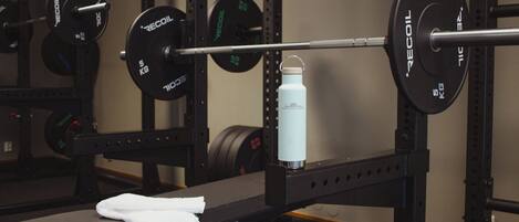 A weightlifting bench with a barbell loaded with weight plates, a water bottle, and a towel.