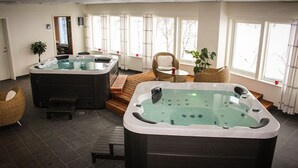 Een spa-ruimte met twee bubbelbaden, een rieten stoel, een bijzettafeltje en een plant.