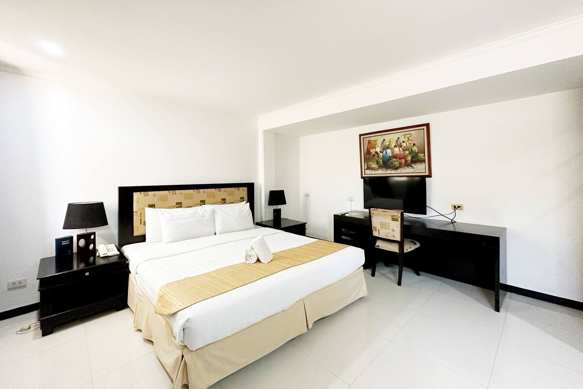 A hotel room with a bed, bedside tables, a desk, and a television.