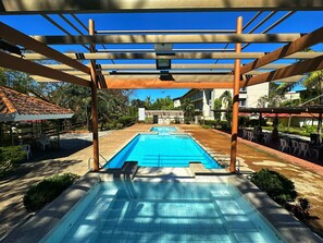 A swimming pool with a pergola overhead, surrounded by outdoor seating and greenery. - Subic Bay Peninsular Hotel (Olongapo)