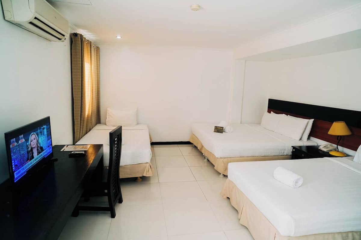 A hotel room with two beds, a desk with a TV, and a window with curtains.