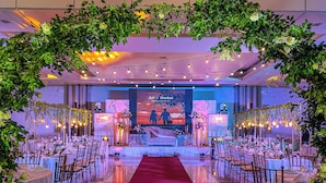 Un salón de bodas con escenario central, alfombra roja y mesas dispuestas con sillas para los invitados.